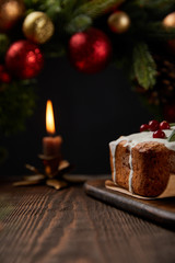 Fototapeta na wymiar selective focus of traditional Christmas cake with cranberry near Christmas wreath with baubles and burning candle on wooden table isolated on black