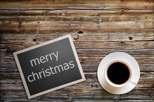 photo with the text merry christmas lies on a wooden table with a cup of coffee