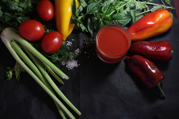 tomato juice and fresh vegetables on a black background