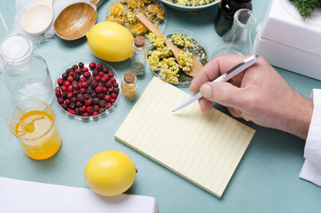 Naklejka na ściany i meble Concept of natural medicine.Doctor writing the prescription fr the patient.Lemons, dried flowers, herbs, berries, blank noteboook on the blue medical table