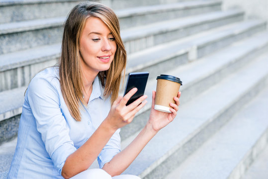 Young smart professional woman reading using phone. Female businesswoman reading news or texting sms on smartphone while drinking coffee on break from work - Powered by Adobe