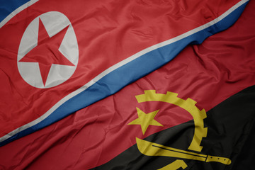 waving colorful flag of angola and national flag of north korea.