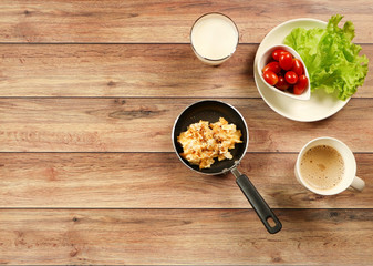 Top view of scramble eggs in pan , vegetable and tomato , cup of coffee ,  milk