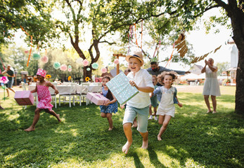 Small children ruunning with present outdoors in garden on birthday party. - obrazy, fototapety, plakaty