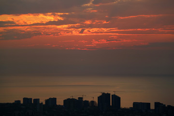 Silhouette of skyscrapers and construction area with sunset sky over the sea in background  