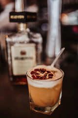 Close up shot of pisco sour cocktail with a dehydrated slice of orange as a garnish. Classic peruvian cocktail, concept of traditional summer drinks. Selective focus on the glass.