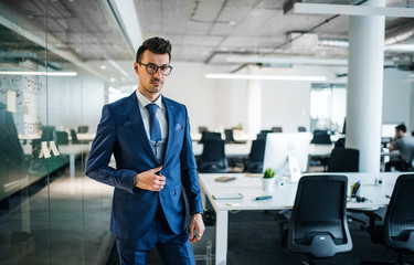 A portrait of young businessman standing in an office, looking at camera.