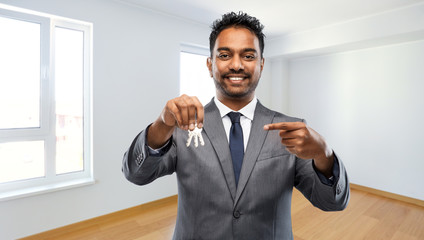 real estate business and people concept - indian man realtor with keys over empty new apartment room background