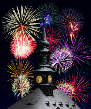 The clock on the town hall tower shows midnight, the background festive fireworks. A colorful fireworks at midnight to celebrate the New Year.