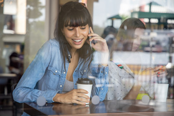 happy hispanic woman, south american latin woman drinking coffee and using smartphone; concept of urban lifestyle in coffee shop with mobile app, smartphone technology, 4G, 5G, internet of things