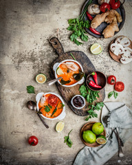 Tom Yum soup with shrimps in bowls on shabby beige background with limes, chili pepper, ginger root and mushrooms, ingredients for cooking, copy space
