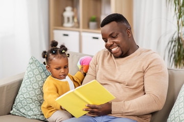 family, fatherhood and people concept - happy african american father reading book for baby...