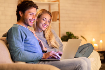Spouses Browsing On Laptop Sitting Relaxing On Sofa At Home