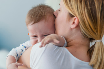 Mother holding crying baby. Young woman with her little son.