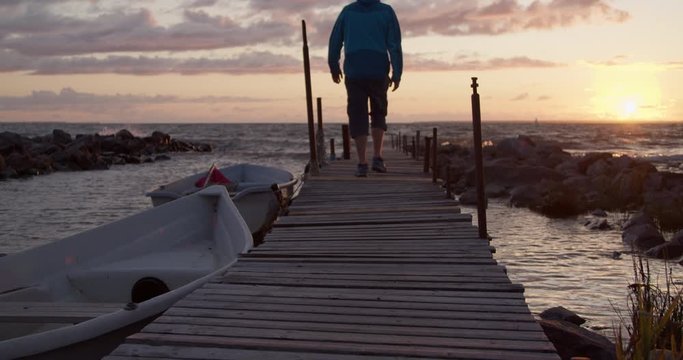 Man walking on wooden dock bridge at sunset in slow motion