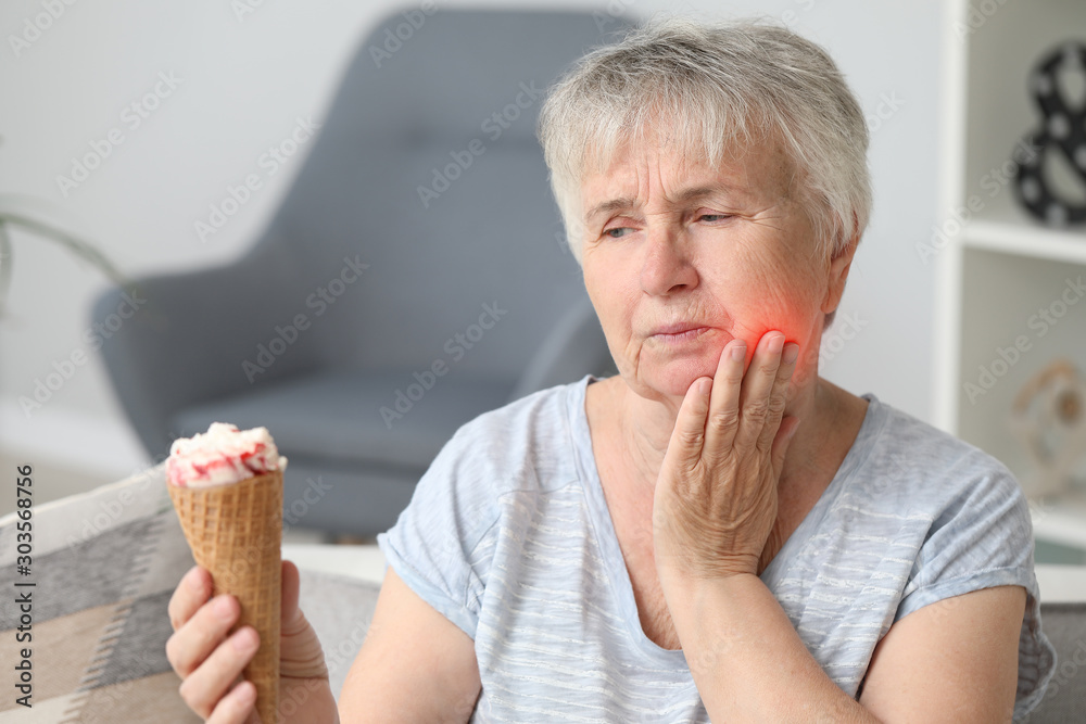 Sticker Senior woman with sensitive teeth and cold ice-cream at home