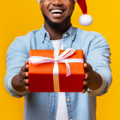 Cheerful afro guy offering Christmas gift box to camera