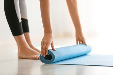 Fototapeta premium Young woman rolling yoga mat at home