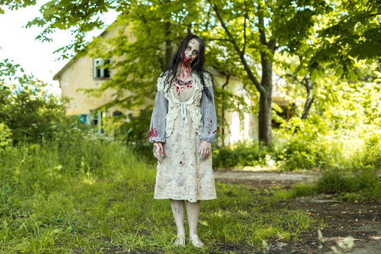 Girl zombie in the blood in the forest on the background of the house