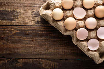 Top view closeup of eggshell and whole eggs in cardboard recycled egg box with copy space on wooden background
