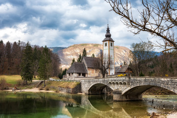 Amazing spring view of Bohinj lake with the church of St John the Baptist and the stone bridge in Triglav National Park, located in Julian Alps, Slovenia.