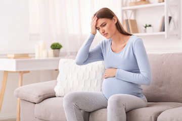 Obraz premium Expectant Woman Touching Head Having Headache Sitting On Couch Indoor