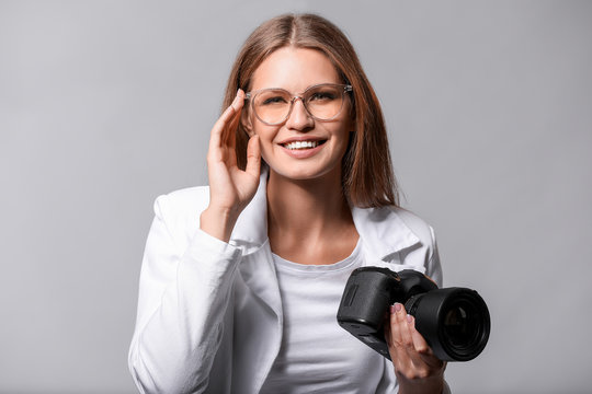 Beautiful female photographer with camera on grey background