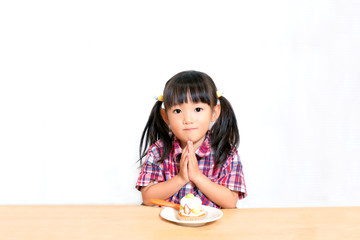 Naklejka premium 白背景でおやつのケーキを食べる前に「頂きます」をする幼い女の子。躾、マナー、行儀、幸せイメージ