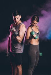 Sporty young couple with dumbbells on dark background