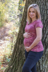 Smiling young pregnant woman is posing in autumnal park. Vertically. 