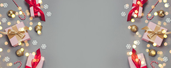 Winter Christmas or New Year banner with paper pink presents and ren ribbons, candy canes, confetti and silver balls on grey background.