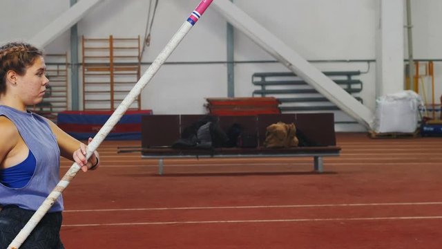Pole vaulting indoors - young woman with pigtails preparing for the jump - running up - jumping over the bar