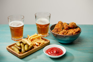 delicious chicken nuggets, ketchup, french fries and gherkins near glasses of beer on turquoise wooden table isolated on grey
