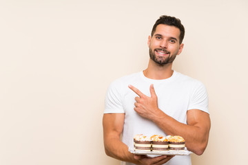 Handsome man holding muffin cake over isolated background pointing to the side to present a product