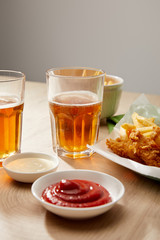 glasses of beer, chicken nuggets with french fries, ketchup and mayonnaise on wooden table on grey background