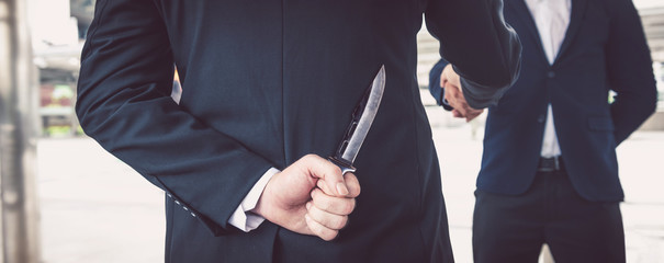 two business making handshake a deal but hiding knives