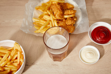 glass of beer, chicken nuggets with french fries, ketchup and mayonnaise on wooden table