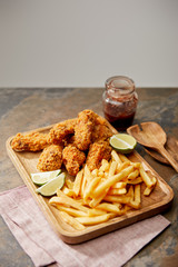wooden board with delicious chicken nuggets, french fries and lime on stone surface isolated on grey