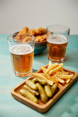 selective focus of delicious chicken nuggets, french fries and gherkins near glasses of beer on turquoise wooden table on grey background