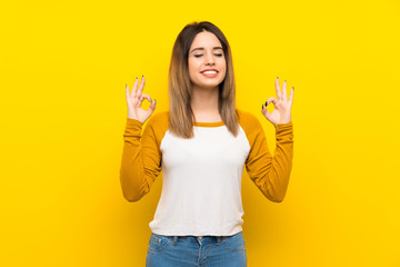 Pretty young woman over isolated yellow wall in zen pose