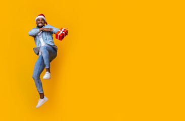 Cheerful black man holding gift box and jumping in air