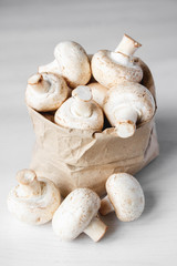 Mushrooms champignons in paper bag on a white wooden table. Place for text or advertising. Top view