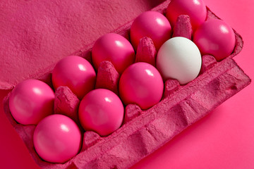 Fototapeta na wymiar White egg among pink ones in package. Concept of uniqueness