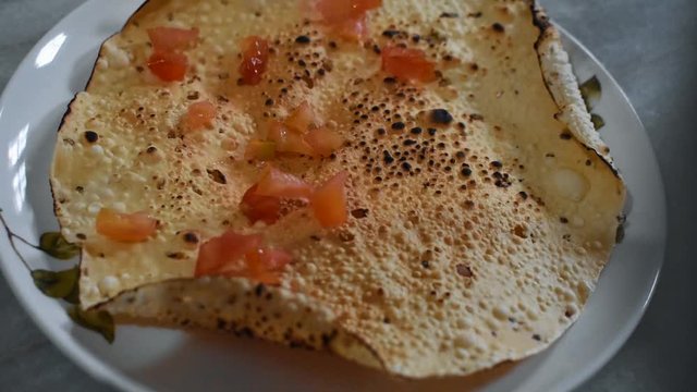 Tomatoes being sprinkled on papad
