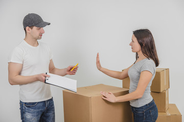 Young delivery guy transported all the cardboard boxes into new flat and is waiting for woman's signature, but she refuses to sign anything untill she check if everything is all right with her things.