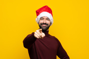 Man with christmas hat over isolated yellow background points finger at you with a confident expression