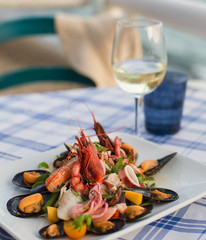 Mixed seafood salad (shrimps, mussels, squids) on the table, located on the beach. Ischia, Italy.