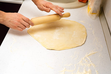 Roll out the dough. baker rolls out the dough on a wooden kitchen table sprinkled with flour