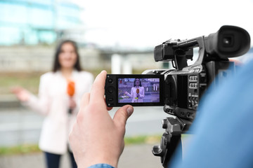 Young male journalist and video operator working on city street, focus on camera display