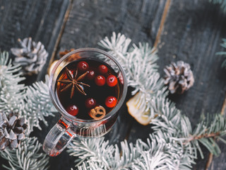 Mulled wine with cranberries on a dark wooden table with Christmas tree branches in the snow